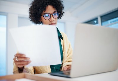 Uma secretária trabalha num documento com um computador na mão e um papel